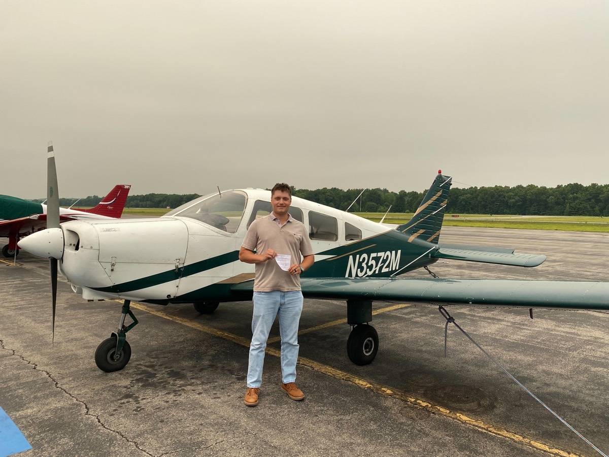 Adam Clark standing on the ramp in front of a white and green Piper airplane, tail number N3572M